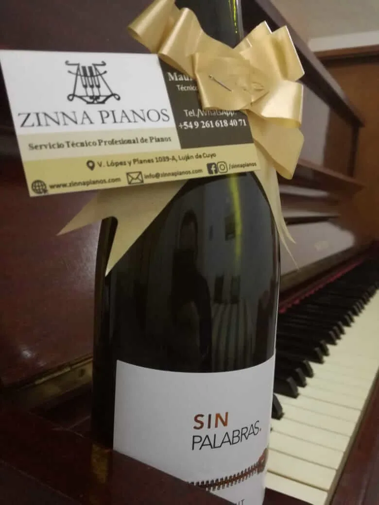 Botella con la tarjeta de Zinna Pianos sobre un piano