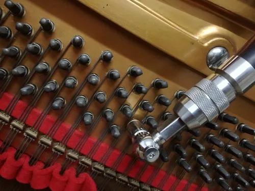 Llave de afinar sobre las clavijas de un piano, con el fieltro rojo de temperar entre las cuerdas